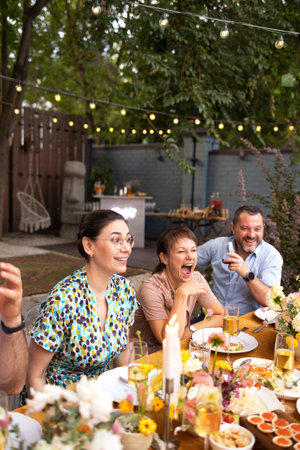 Many people saying cheers and showing their champagne glasses full of sparkling wine to each other whilst enjoying an outdoor wedding party on a backyard restaurant at sunsetの写真素材