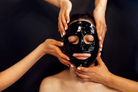 Beautiful caucasian woman with black silicone mask for the skin. Pretty brunette female with cosmetic mask on her face. Skin care cosmetics on background. Dark black drop. copy spaceの写真素材