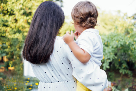 Lovely portrait of a beautiful mother kissing her little son. Close up of a young brunette female touching her cute child. green leaves in the background. copy space. back viewの写真素材