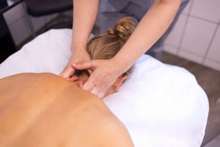 Happy young caucasian girl getting back massage in spa salon. Neat hands of female masseuse with orange manicure. Beautiful smiling woman gets relaxation. copyspace.の写真素材