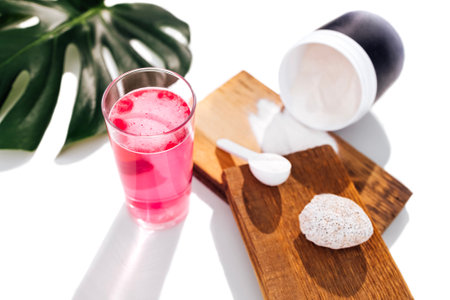 Mockup of plastic jar for collagen powder. Spoon with collagen on wooden stages, glass cup and monstera leaf on the background. Concept of natural organic cosmetic and beauty, dermatology.の写真素材