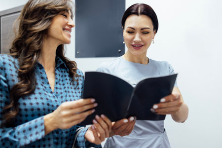 Smiling female client communicates with rcosmetologist woman in a beauty salon. Young pretty caucasian girl signs up for a spa treatment.の写真素材
