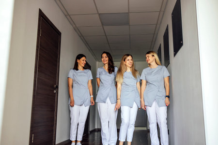Beautiful smiling female doctors in medical uniform stands near the window in clinic. Young nurses is walking. Sunny day. light interior. copyspace.の写真素材