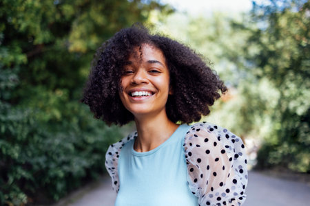 Happy african american teen girl in casual clothes. Smiling darkskin female teenager walking in the park. summertime. green trees on background. copyspace.の写真素材