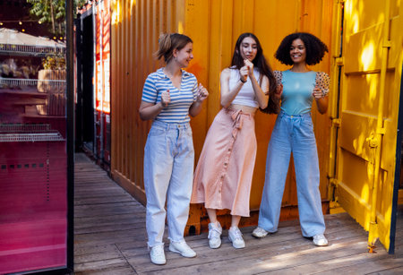 Three cute teenage girls in casual clothes on background of multi colored shipping containers in...