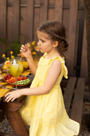 Portrait of little girl drinking juice in a glass, decorated with fruits, with straw at outdoor park. child in summerの写真素材