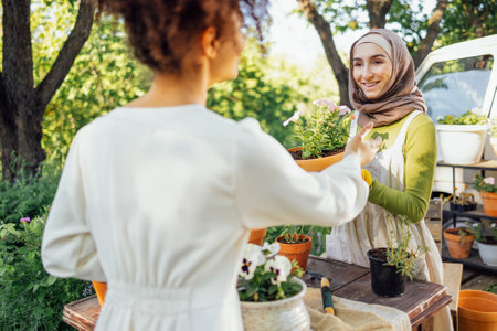 Muslim young attractive gardener at work, take care of green plants, working in retro garden shop with afro american female clientの写真素材