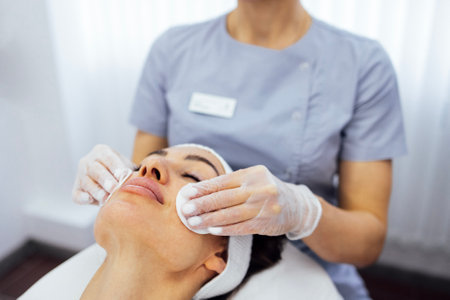 Close up of beautiful young brunette woman during facial cleansing and massage. Cosmetic procedures in a beauty salon or clinic. Lighted candles on background. Skin care and health concept.の写真素材