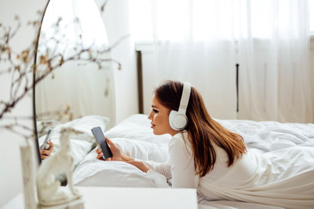 Young beautiful woman in modern wireless headphones relaxing and listening to music. Happy calm white female resting on cozy sofa. Brunette girl put her hands behind her head. light home backgroundの写真素材