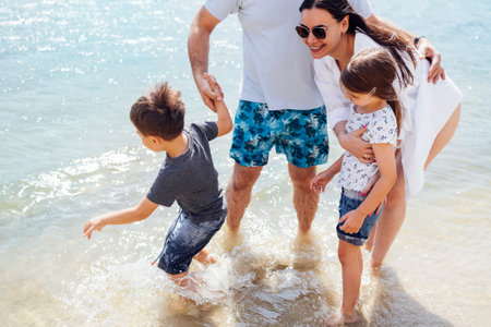 Happy family on the lake or river. Son and daughter run on the water and splash on their smiling parents. Everyone is laughing and having a great time. Free space for text.の写真素材