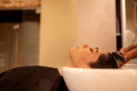 Cheerful young brunette womn enjoying head massage and washing hair while getting her haircareの写真素材