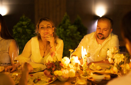 Many people saying cheers and showing their champagne glasses full of sparkling wine to each other whilst enjoying an outdoor wedding party on a backyard restaurant at sunsetの写真素材