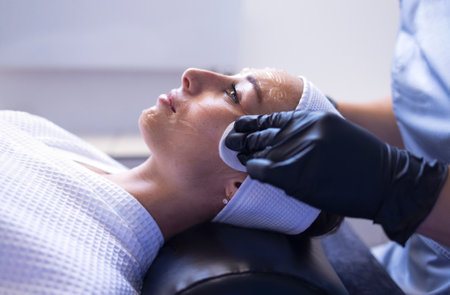 Close up of beautiful young brunette woman during facial cleansing and massage. Cosmetic procedures in a beauty salon or clinic. Lighted candles on background. Skin care and health concept.の写真素材