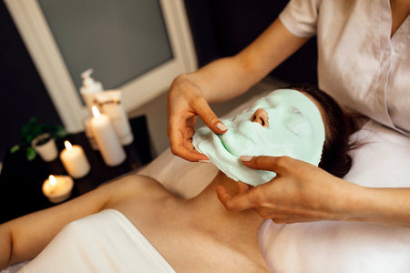 Facial Skin Treatment. Beautiful Young Woman Receiving Cosmetic Mask In Beauty Salon. Beautician Applying Alginate Mask On Female Face With Smooth Soft Skinの写真素材