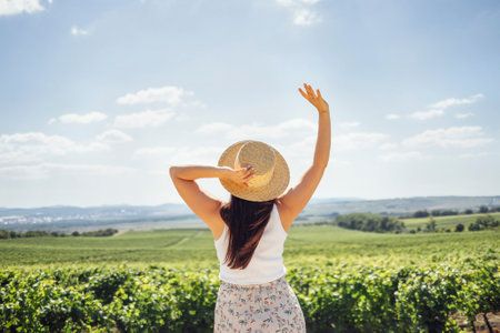 Happy young woman walking through the vineyard. White female in casual clothes and straw hats look at the landscape. Happiness and travel concept. copyspace.の写真素材