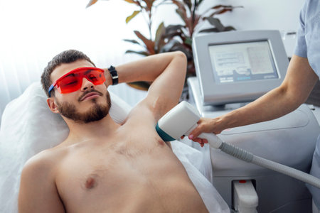 Young man receiving photo epilation while visiting beauty center at salon, professional female beautician doing laser hair removal procedure on clients face. Cosmetology conceptの写真素材