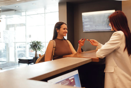 Young brunette woman in sportswear taking the sport bracelet while standing in front of window at gym at reception area. Female receptionist smiling to herの写真素材