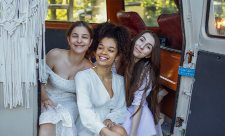 Pretty smiling three teenage girls in light dresses. Female teens of different nationalities sit at...