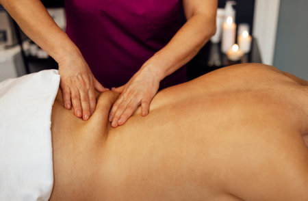 Happy young caucasian girl getting back massage in spa salon. Neat hands of female masseuse with orange manicure. Beautiful smiling woman gets relaxation. copyspace.の写真素材