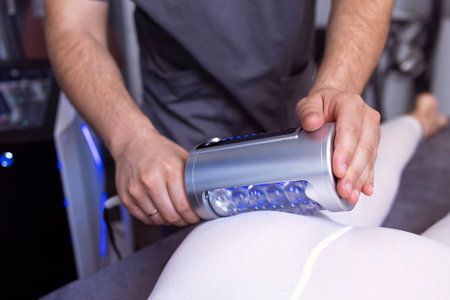 Faceless beautician using massager to remove fat from hips of anonymous customer in salon....