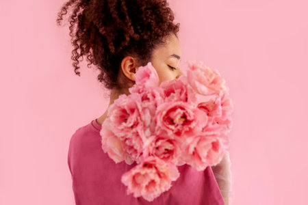 Beautiful african girl holds a bouquet of pink flowers near her face. Gentle female studio portrait...