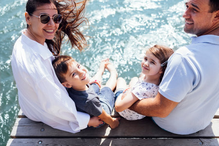 Happy family on wooden bridge against the backdrop of the sea or lake. Mom hugs her son. Dad hugs his daughter. view from the back. copyspace.の写真素材
