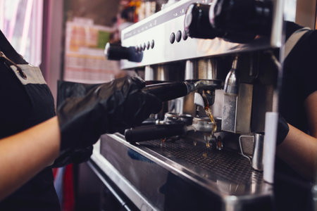 Barista in black gloves and apron rinses the holder of automatic coffee machine before preparing the next cup of coffee. Takeaway cafe interior. close up. copyspace.の写真素材