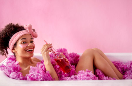 Attractive young female african with terry headband and patches under her eyes is sitting in bath on...