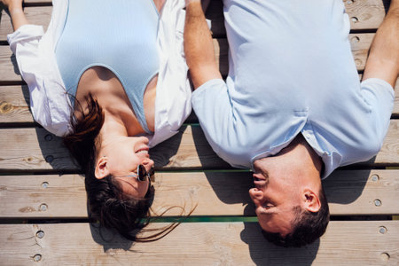 Young couple in love in light casual clothes is lying on wooden bridge. Happy woman and man hug and laugh on the background of sea or river water. love story. view from the back.の写真素材