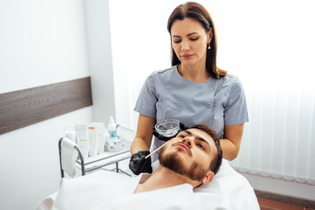 Beauty salon beautician applies cooling gel to clients skin. Preparing the skin of young man for laser hair removal of the cheek. Close up of brunette male in clinicの写真素材