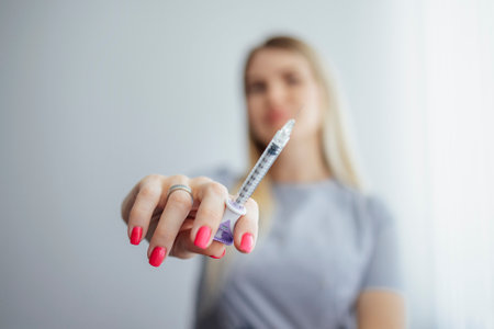 Close up of woman in medical gloves holding syringe with clear liquid. White background with female...