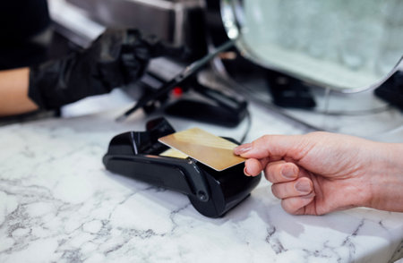Close up of female hand of the client makes contactless payment with bank card. Another woman's hand...