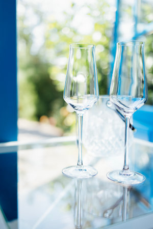 Close up of empty champagne glasses on transparent table. Ice cooler and blue door in garden with green trees on background. Waiting for meeting and romantic dinner or holiday date celebration.の写真素材