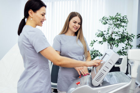 Woman cosmetologist touches screen of cosmetology equipment to set necessary parameters and teaches...
