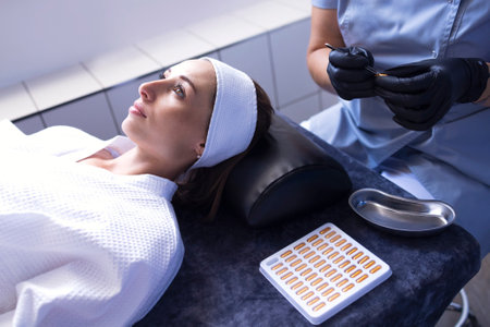 Close up of beautician applies ampoule cream in black gloves to face of female client in spa salon....