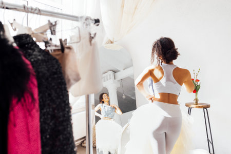 Charming smiling cute african girl in white top and leggings by trempels with stylish clothes. Laughing attractive young afro woman choices of clothing on rack. Shoppingの写真素材