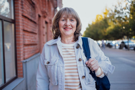 Middle aged attractive blond woman student with curly hair in stylish denim clothes, walking in city. education and study conceptの写真素材