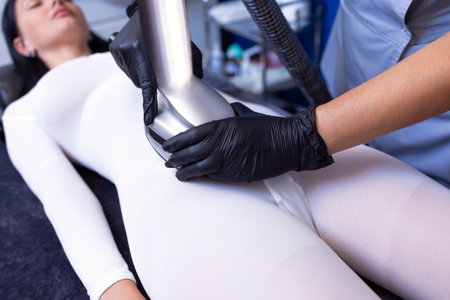 Master makes lymphatic drainage to the client in a special white costume in the abdomen. Close up of apparat procedure for weight loss. Lpg massage with cream. copy spaceの写真素材