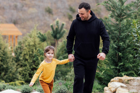 Young laughing man holds the hand of little cute girl. Smiling dad together with his sweet daughter in the park. Happy family having fun outside the city. copyspace.の写真素材