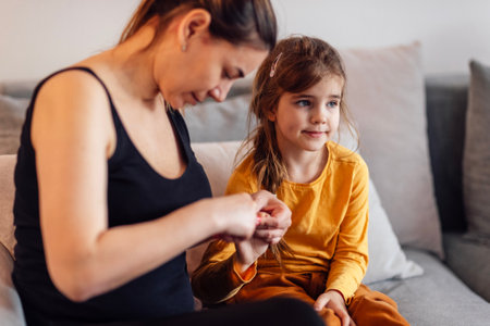 Young mother trims the nails on the hands of her cute daughter with small baby scissors. Loving mom cuts off long nails of little female kid at home. Children care and hygiene concept.の写真素材