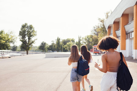 Group of teenagers of different nationalities and appearance have a fun together. Young and positive student girls in casual clothes with backpacks laugh and chat on the street. friendship concept.の写真素材