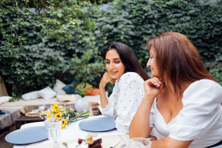 Young attractive girl talking to her mother on terrace of house in garden. Two smiling women in...