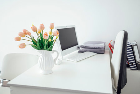 a workplace with a computer, a keyboard, folders with documents and a jug with tulips. Modern style interior. A place for a doctor to work with a white table and two chairs. no people. copyspace.の写真素材