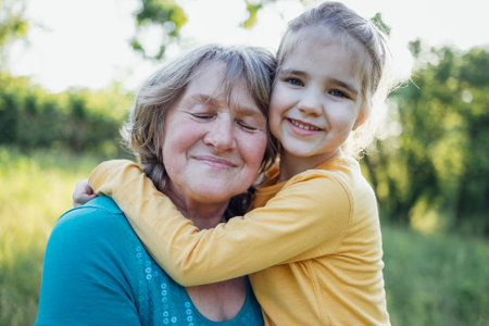 Little girl hugging smiling middle aged woman. Cute female kid and her grandmother enjoy walking outdoors. Granny and her granddaughter having great time together. Joyful meetings of family members.の写真素材