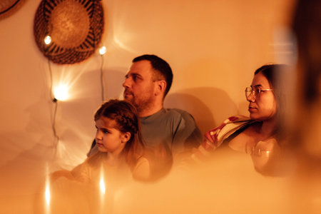 Happy family watches TV in the evening in their living room. A young mom, dad and their cute daughter are watching a movie at home. Cute little girl and her parents spend time together.の写真素材