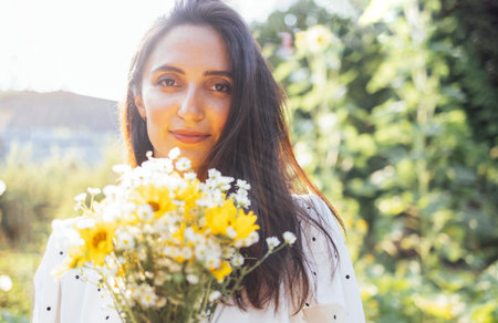 Charming multiethnic girl in casual clothes holds a beautiful bouquet of flowers against the background of green trees and hills. Attractive young woman outdoors in a park or garden. copy space.の写真素材
