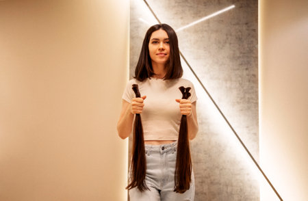 Smiling attractive girl holds bundles of cut hair in her hands. A young charming female brunette in...