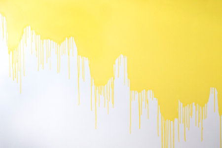 A half painted concrete white wall. Streams and drops of yellow paint on a white background. Spots of paint. Abstract background.の写真素材