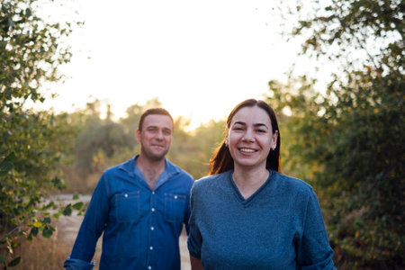 Young married couple holding hands goes along sandy road. Romantic man and woman in casual clothes on a walk in the autumn forest. Husband and wife spend time together.の写真素材