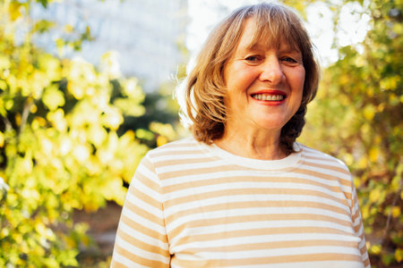 Portrait of handsome senior woman standing by the autumn park. Smiling elderly lady in outdoor...